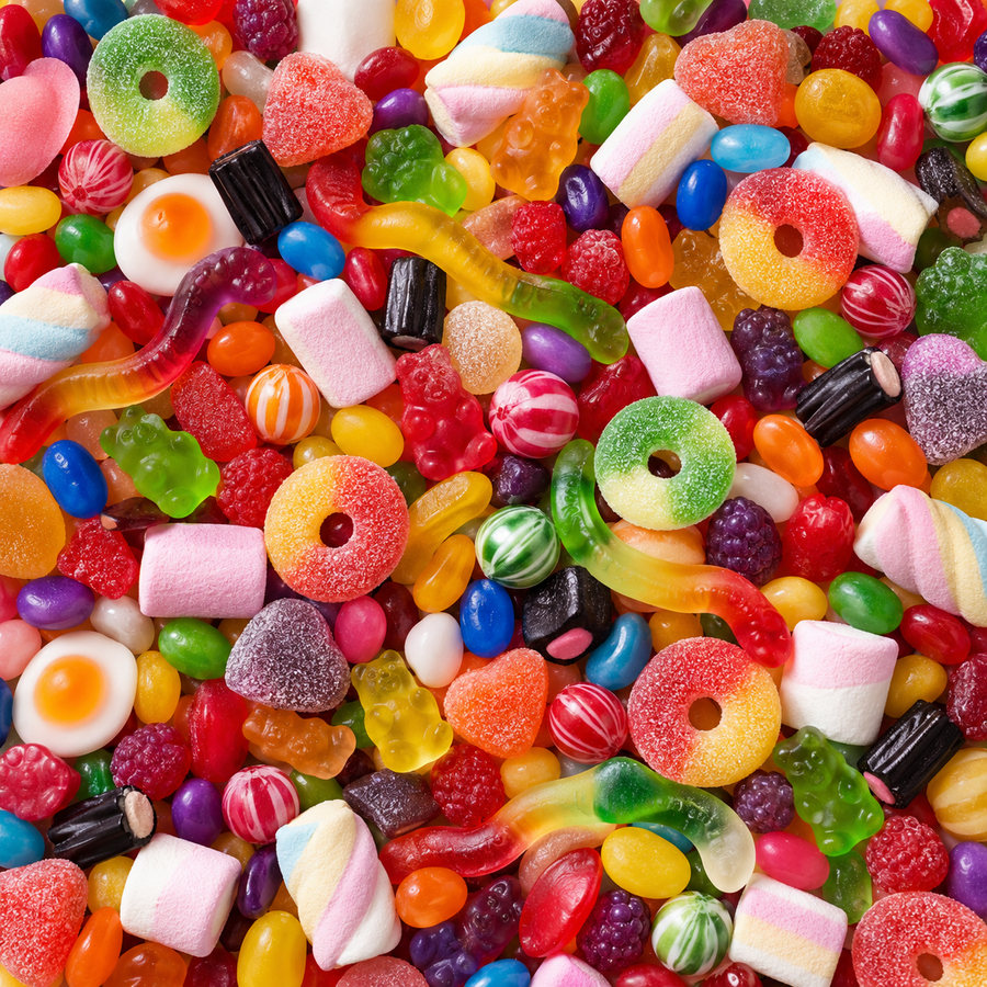 A dense, close-up pile of assorted colorful candies including gummy bears, sour rings, jelly beans, marshmallows, gummy worms, and hard candies filling the entire frame.